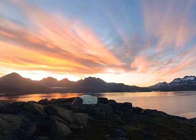 Ein einsames Zelt inmitten der Wildnis Ostgrönlands vor einer wunderschönen Lichtstimmung zum Sonnenuntergang